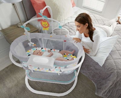 baby sleeping in Fisher-Price Soothing Motions Bassinet near the mom