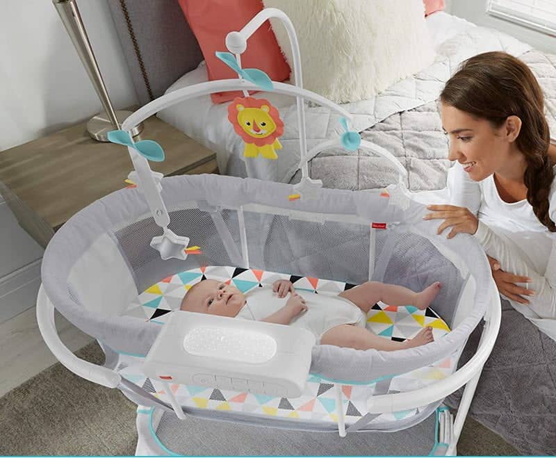 Mom sitting near the bed of Fisher-Price Soothing Motions Bassinet