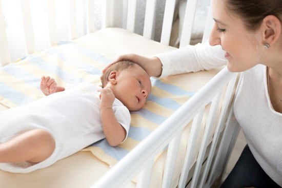 mom sitting near the crib of newborn baby